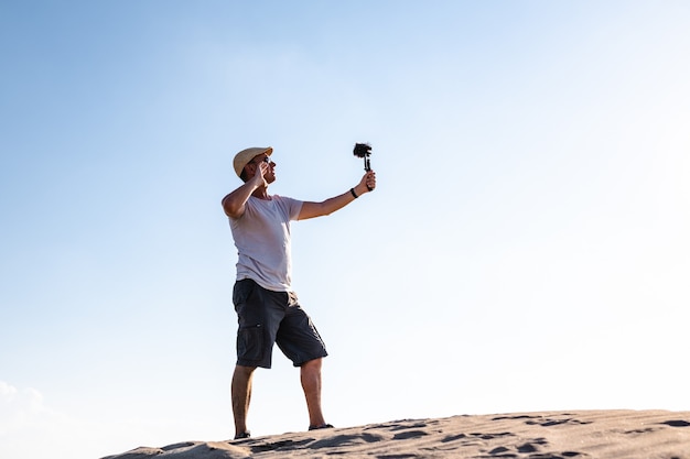 Widok z boku podróżnika stojącego na wydmie i filmującego treści dla mediów społecznościowych