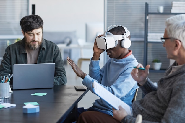 Widok z boku portret afroamerykańskiego mężczyzny noszącego zestaw VR podczas spotkania z różnorodnym zespołem IT w biurze