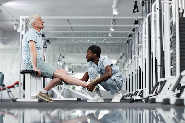 Widok z boku portret afroamerykańskiego młodego medyka badającego starszego mężczyznę w sali gimnastycznej