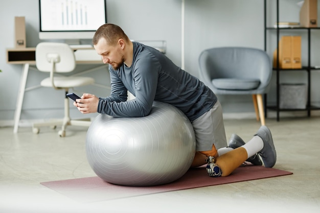 Widok z boku portret dorosłego mężczyzny z protezą nogi ćwiczącej z piłką fitness w domu i używającej s