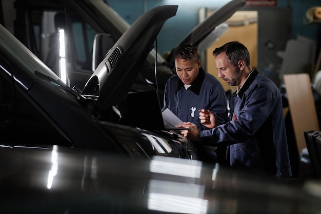 Widok z boku portret dwóch mechaników korzystających z laptopa podczas kontroli samochodu w garażu z kopią światła akcentującego