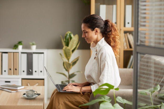 Widok z boku portret eleganckiej bizneswoman za pomocą laptopa siedząc na kanapie w biurze, kopia przestrzeń
