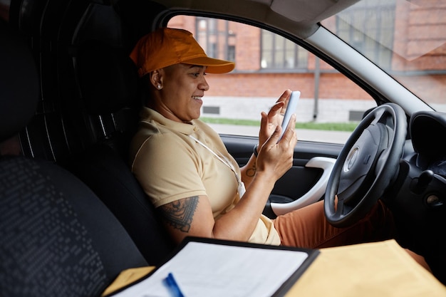 Widok z boku portret kobiecego kierowcy dostawy za pomocą aplikacji na smartfona w vanie