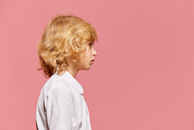 Widok z boku portret małego chłopca z kręconymi blond włosami w białej koszuli pozowanie na różowo