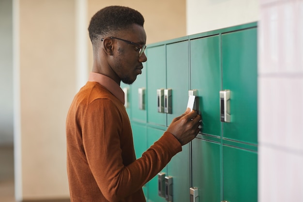 Widok z boku portret młodego mężczyzny African-American otwarcia szafki w kolegium lub budynku biurowym, kopia przestrzeń