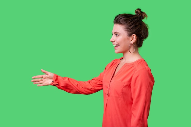 Zdjęcie widok z boku portret pięknej eleganckiej kobiety z fryzurą kok, dużymi kolczykami i stojącą czerwoną bluzką, podając rękę na powitanie lub uścisk dłoni. studio strzał na białym tle na zielonym tle