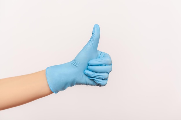 Widok z boku profilu zbliżenie ludzkiej dłoni w niebieskich rękawiczkach chirurgicznych pokazujących jak lub kciuki do góry.