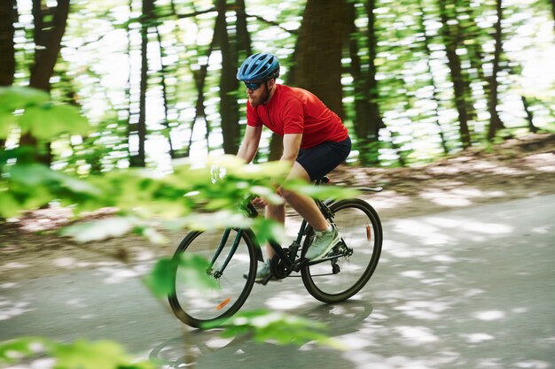 Widok Z Boku. Rowerzysta Na Rowerze Jest Na Asfaltowej Drodze W Lesie W Słoneczny Dzień