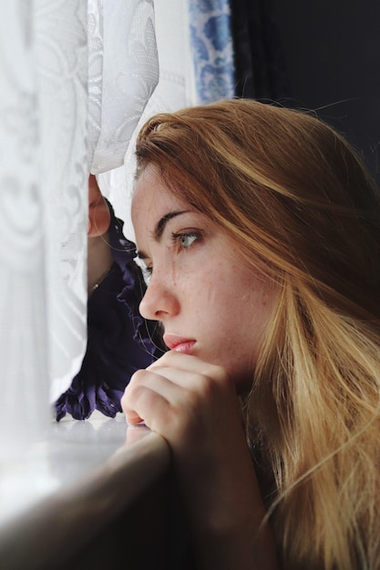 Widok z boku rozmyślnej nastolatki patrzącej przez okno