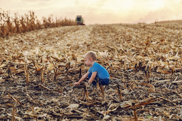 Widok z boku ślicznego chłopca rolnika, skulonego na polu kukurydzy i grającego