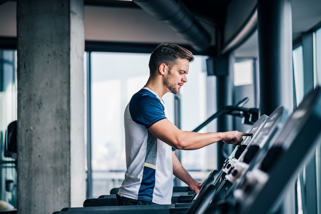 Widok z boku sportowca, dostosowując prędkość na bieżni, robi treningu cardio na siłowni.