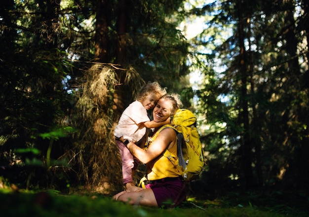 Widok z boku szczęśliwa matka z małą córeczką na zewnątrz w letniej przyrodzie, przytulanie i odpoczynek.