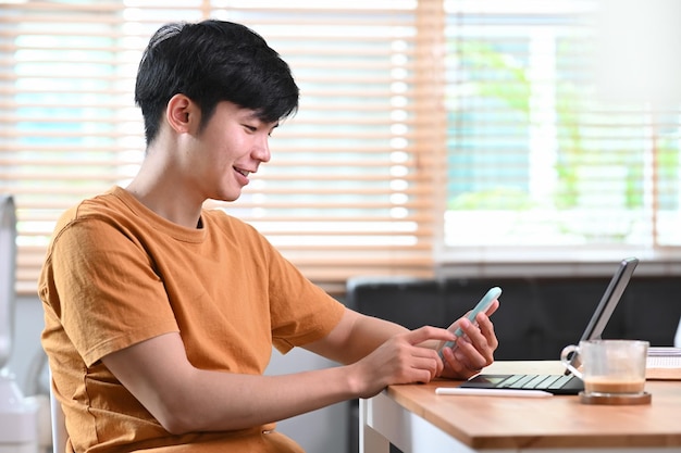 Widok z boku uśmiechnięty przypadkowy mężczyzna siedzący w salonie i używający smartfona