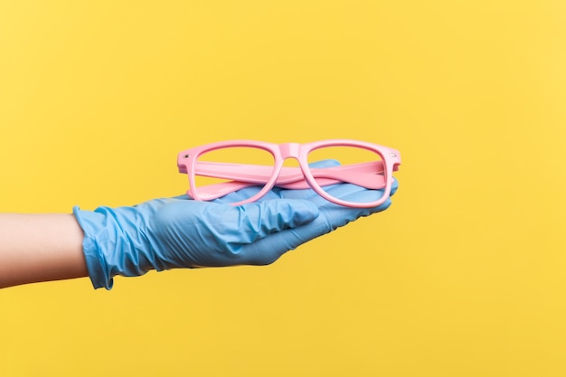 Widok z boku zbliżenie ludzkiej ręki w niebieskie rękawiczki chirurgiczne, trzymając i dając różową ramkę okularów.