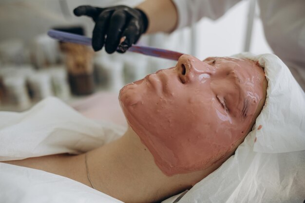 Zdjęcie widok z boku zbliżenie relaksujący piękna młoda kobieta azjatyckich cieszyć się relaksem podczas robienia peelingu twarzy maska do pielęgnacji skóry zabieg kosmetyczny spa przez kosmetyczkę w centrum salonu spa