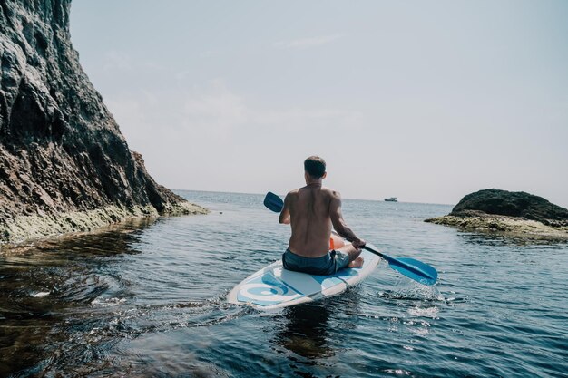 Widok z boku zdjęcia mężczyzny pływającego i relaksującego się na desce sup, sportowego mężczyzny w morzu na stoisku