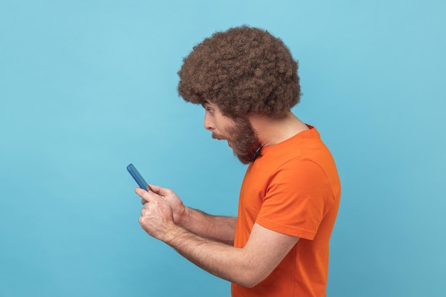 Widok z boku zdumionego mężczyzny czytającego post w sieci społecznościowej za pomocą czatu telefonicznego wyglądającego na zaskoczonego