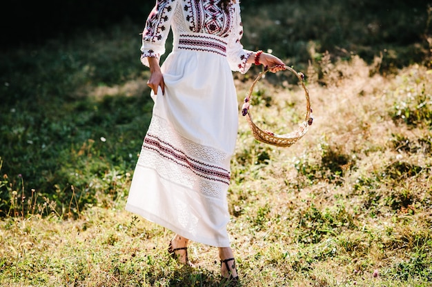 Zdjęcie widok z dołu dziewczyna z kwiatami w koszu spacer w parku, przygotowanie druhny na wesele w ogrodzie, na podwórku, na zewnątrz. ukraiński styl rustykalny: panna młoda w haftowanej sukience o charakterze.