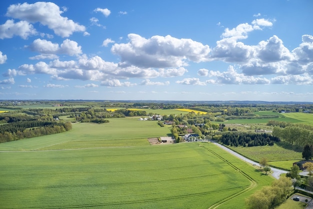 Widok z drona na pola uprawne i pola uprawne na zewnątrz w Europie latem lub wiosną Żywe i jasne pastwiska rosnące na niekończących się polach uprawnych z niebieskim tle nieba nad rozległą i otwartą łąką