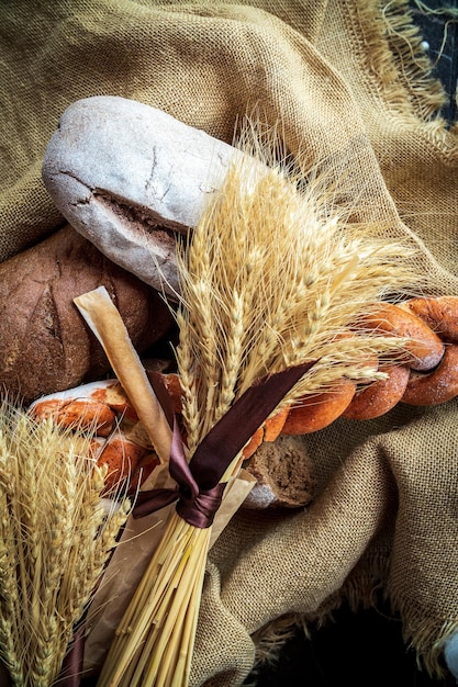 Widok z góry bukietu pszenicy leżącego na świeżym chlebie i innych produktach piekarniczych jako symbol żywności i dobrobytu agrarnego kraju