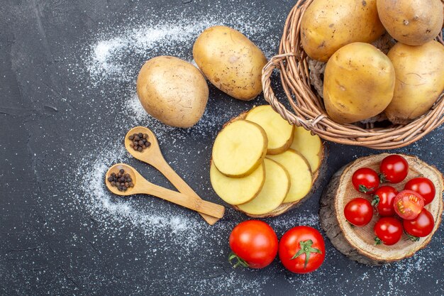 Zdjęcie widok z góry całych i posiekanych świeżych ziemniaków i pomidorów na drewnianej papryce po lewej stronie na czarno-białym tle mix kolorów