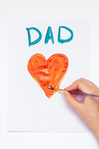 Widok z góry dłoni dziecka rysunek czerwone serce z kartą z życzeniami tata słowo na białym papierze. Koncepcja rodziny i dzień ojca.