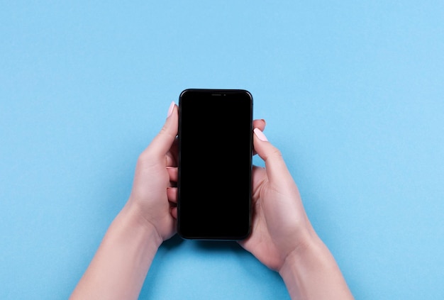 Widok z góry dłoni kobiety używającej iPhone'a na niebieskim tle