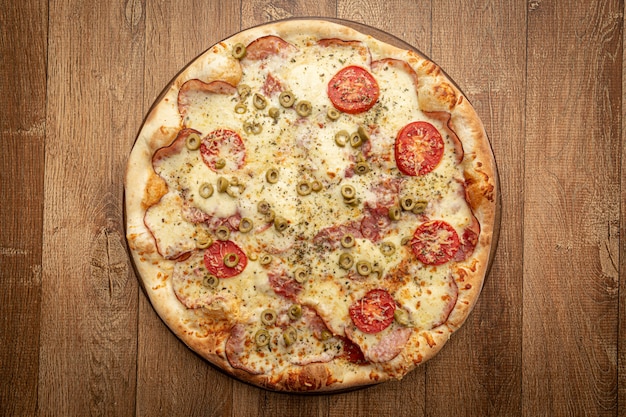 Widok z góry domowej roboty pizzy z pomidorem, oliwką, serem i innymi składnikami.
