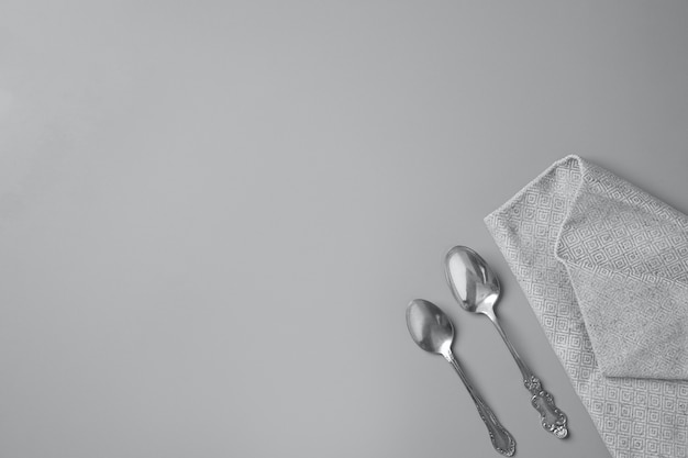 Zdjęcie widok z góry dwóch srebrnych łyżek i szarej serwetki na szaro