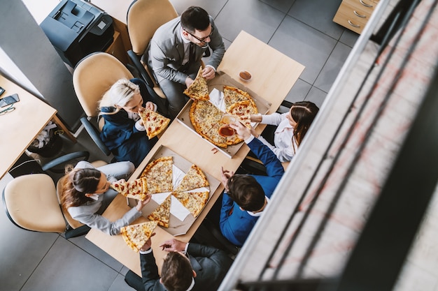 Widok z góry głodnych kolegów siedzących przy stole i jedzących pizzę na lunch. Firmowe wnętrze firmowe.