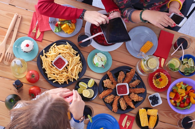 Widok z góry grupy ludzi jedzących razem obiad siedząc przy drewnianym stole. Jedzenie na stole. Ludzie jedzą fast foody.