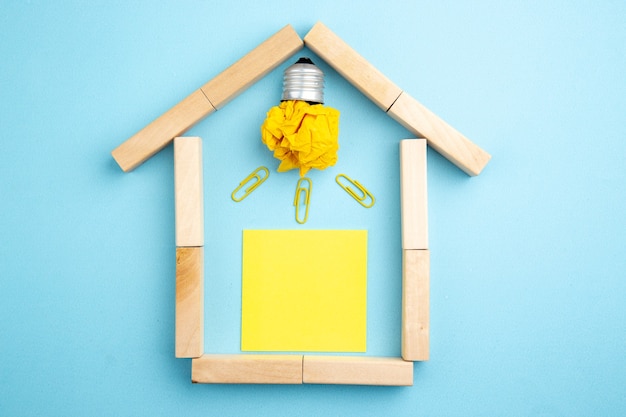 Zdjęcie widok z góry idealna żarówka i żółta karteczka samoprzylepna w drewnianych blokach w kształcie domu na niebieskim tle