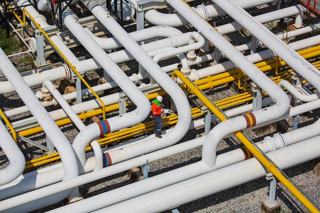 Zdjęcie widok z góry inspekcja męskiego pracownika na stalowych długich rurach i zaworze kolankowym w stacji olejowej podczas zaworu rafineryjnego wizualnej kontroli oleju rurociągu