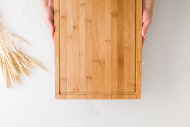 Zdjęcie widok z góry kobiecych rąk trzymających drewnianą deskę w marmurowym stole z pszenicy i mąki z miejscem na tekst