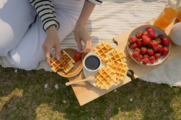 Widok z góry kobiety jedzącej śniadanie z waflami i truskawkami na drewnianej tacce
