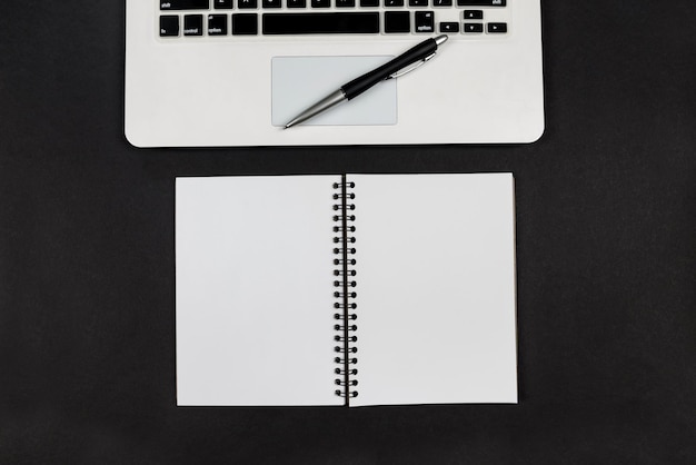Zdjęcie widok z góry laptopa z notatnikiem i długopisem na czarnym tle