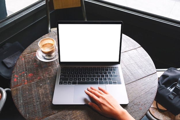 Widok z góry makieta obraz kobiety używającej i dotykającej touchpada laptopa z pustym białym ekranem pulpitu na drewnianym stole