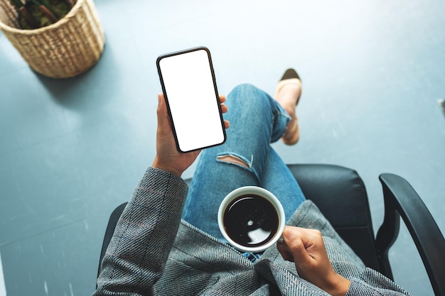 Widok z góry makieta obrazu kobiety trzymającej telefon komórkowy z pustym białym ekranem pulpitu z filiżanką kawy