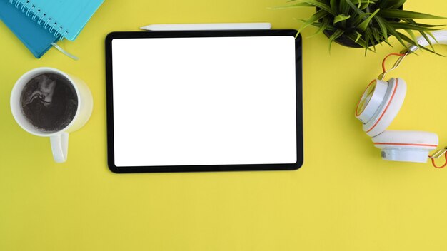 Widok z góry makiety cyfrowego tabletu, słuchawek, filiżanki kawy i roślin na żółtym tle.