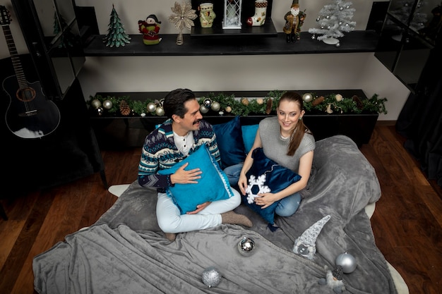 Widok z góry młodej pary rozmawiającej radośnie w salonie z poduszkami i kocem w noc Bożego Narodzenia.