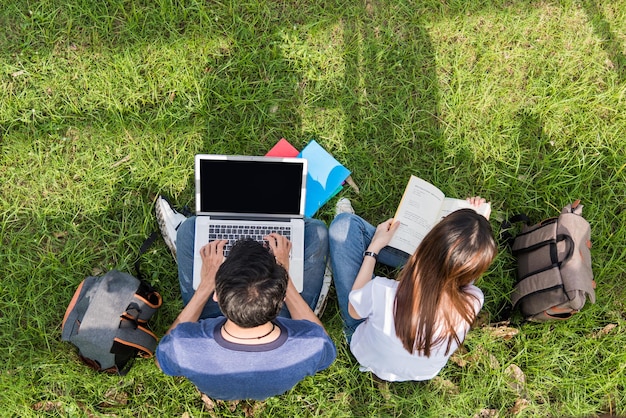 Widok z góry młodzi studenci siedzący na trawie z laptopem i książką konsultują się razem