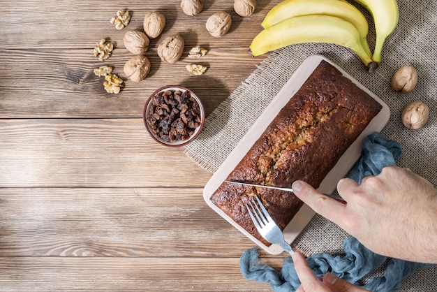 Zdjęcie widok z góry na cięcie chleba bananowego z orzechami, rodzynkami i bananami na rustykalnym drewnianym tle