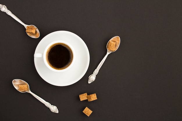 Widok z góry na czarną kawę w białej filiżance i łyżki z brązowym cukrem na czarno