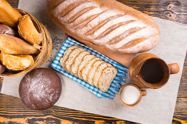 Widok z góry na drewniany dzban, mały kubek mleka i różne bochenki chleba i kromki obok kosza na stole