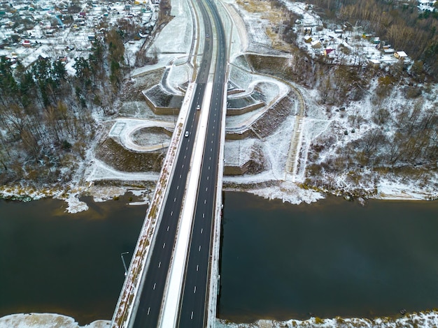 Widok z góry na jezdnię w zimie Zaśnieżona droga i pobocze Autostrada przebiega przez las i sektor prywatny Szczegółowe zdjęcia z drona infrastruktury drogowej