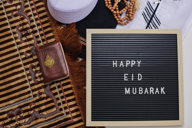 Widok Z Góry Na Muzułmańską Sukienkę I Koraliki Modlitewne Ze świętą Księgą Al Koranu I Tablicą Z Napisem Happy Eid Mubarak Istnieje Arabska Litera, Która Oznacza świętą Księgę