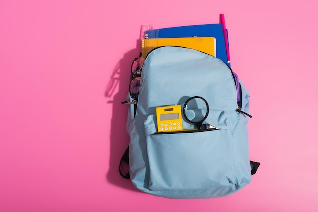 Widok z góry na niebieski plecak z okularami kalkulatora notebooków i przyborami szkolnymi na różowo