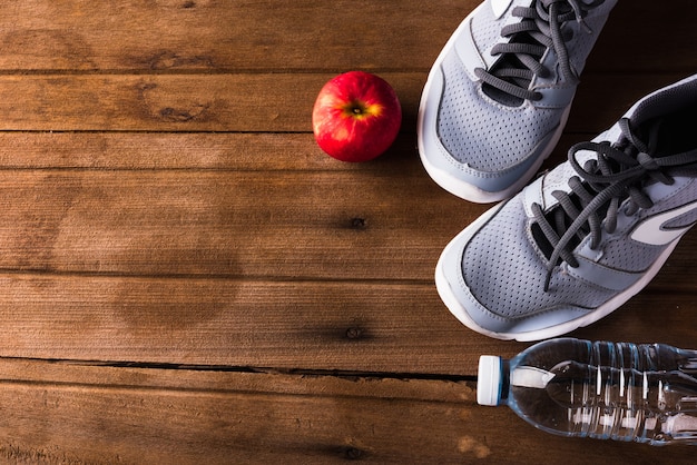 Widok z góry na parę butów sportowych, butelka wody i czerwone jabłko