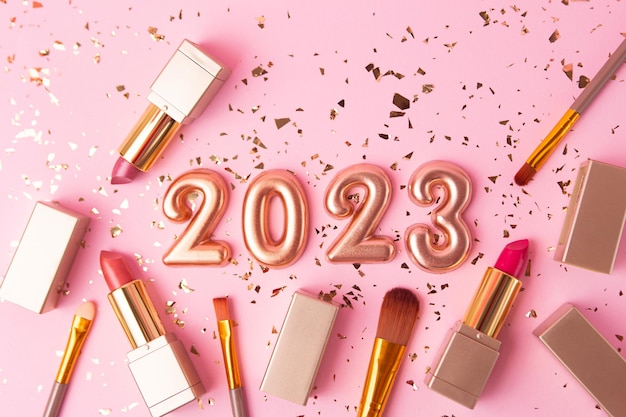 Widok z góry na pędzle kosmetyczne i szminkę na różowym tle Różowe złote cyfry 2023