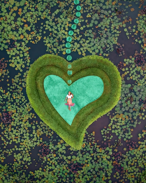 Zdjęcie widok z góry na plantację na ziemi z liliami wodnymi i sercem otaczającym leżącą kobietę